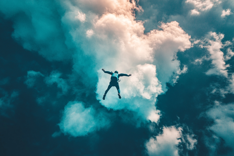 Personne en chute libre lors d'un saut en parachute, entourée de nuages et de lumière, illustrant l'émotion et l'adrénaline de l'expérience.
