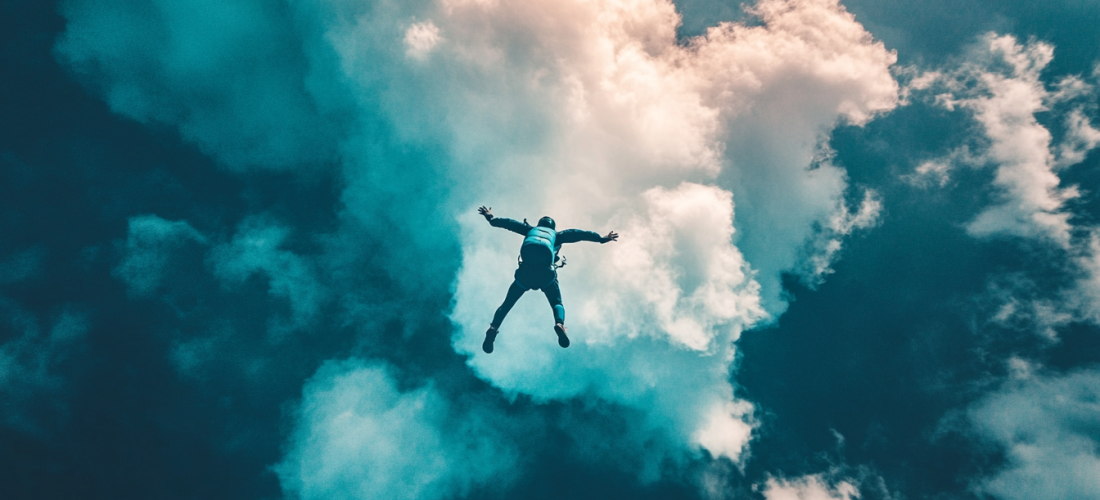 Personne en chute libre lors d'un saut en parachute, entourée de nuages et de lumière, illustrant l'émotion et l'adrénaline de l'expérience.